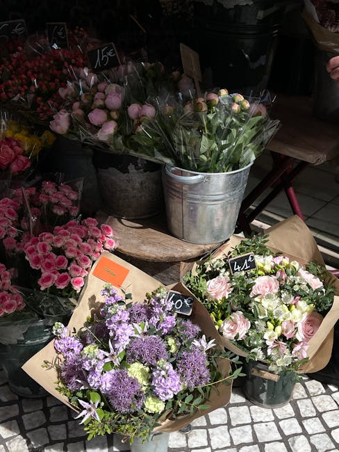 A display of freshly arranged floral bouquets at a flower shop featuring pink roses, purple statice and other blooms wrapped in brown paper, with some flowers in metal buckets and others in plastic co