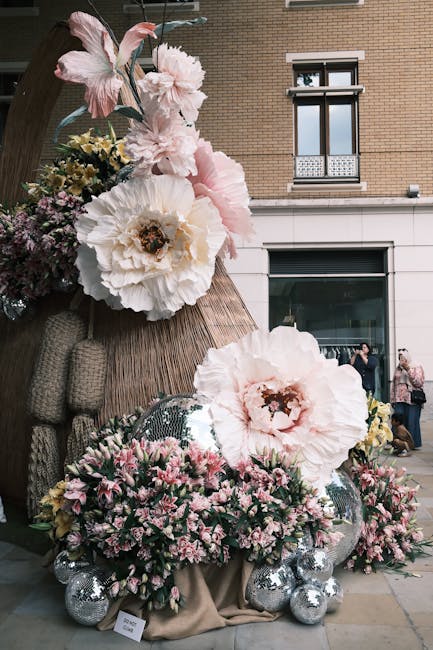 A large floral arrangement featuring oversized, soft pink peonies and white roses with dark centers, complemented by smaller pink and purple filler flowers. The flowers are arranged with green foliage